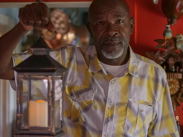An old black man wearing a short-sleeve An older man holding a lantern